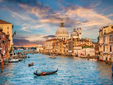 Traditional Gondola On Famous Canal Grande With Basilica Di Santa Maria Della Salute In Golden Evening Light At Sunset In Venice Italy 