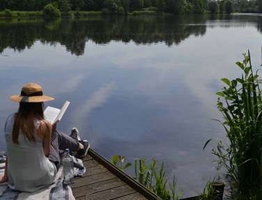 Women reading a book on a jetty over a peaceful lake