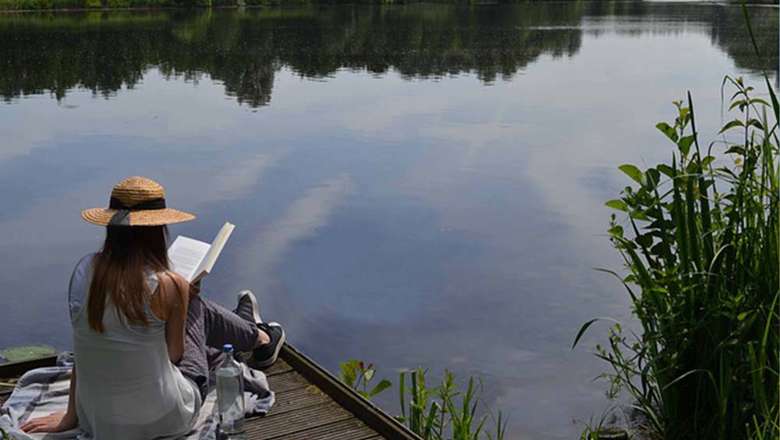 Women reading a book on a jetty over a peaceful lake